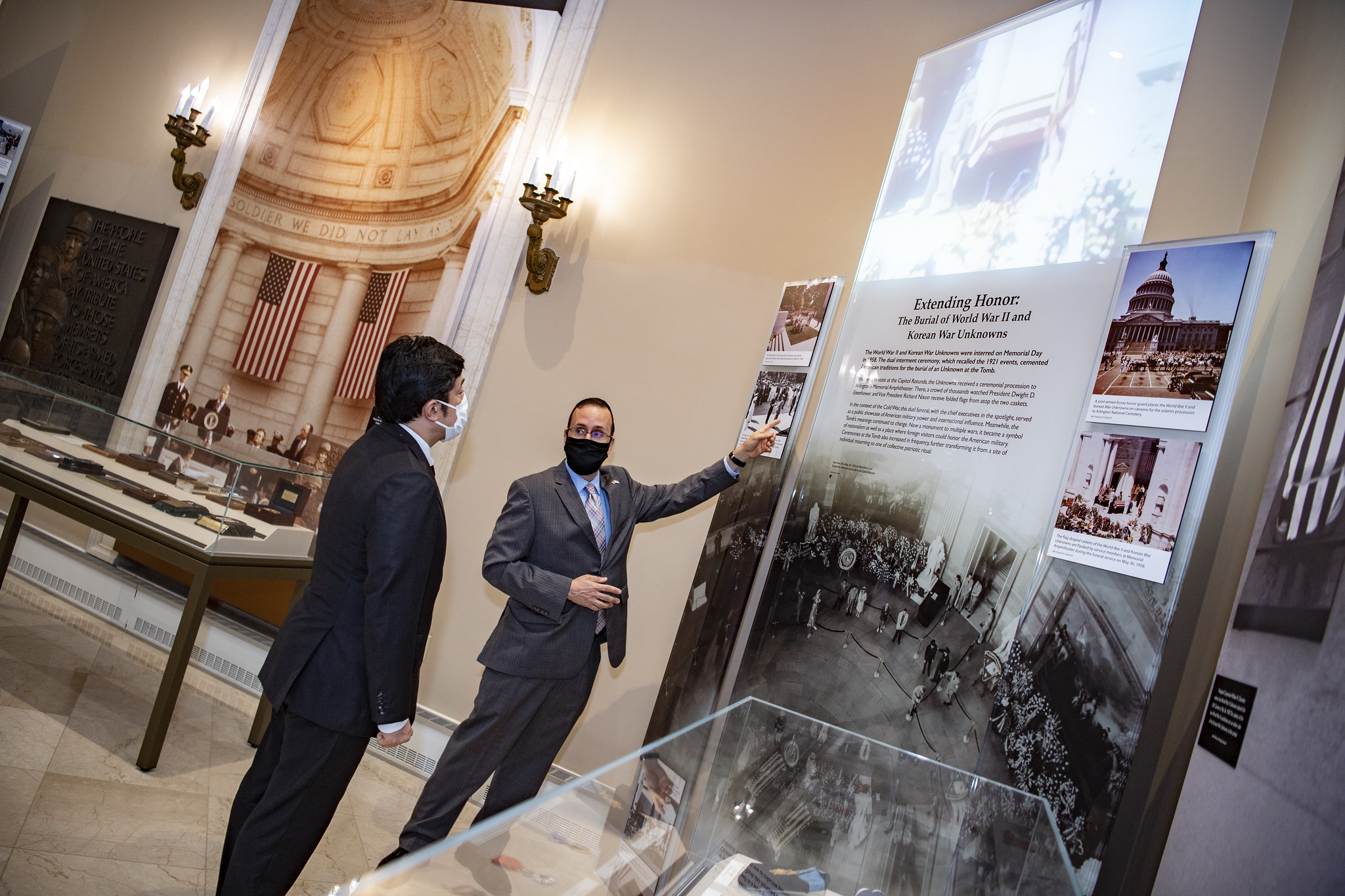 Tim Frank (right), historian, giving a tour of the Memorial Amphitheater Display Room exhibit to State Minister of Defense of Japan Nakayama Yasuhide (left) on August 10, 2021. One of the large glass panels with text, images, and original motion picture footage being projected on to it can be seen.