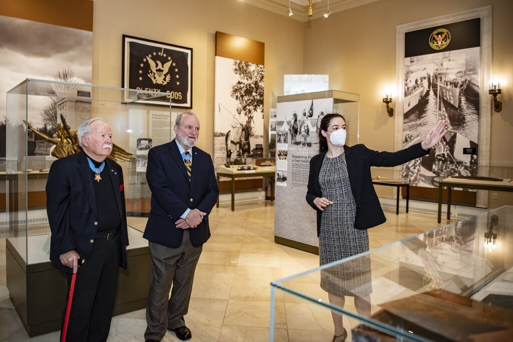 A masked woman shows an exhibit to two men.