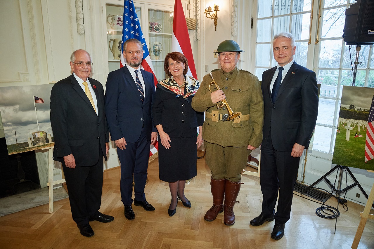 5 people, including a WWI interpreter, stand in a building in front of two flags