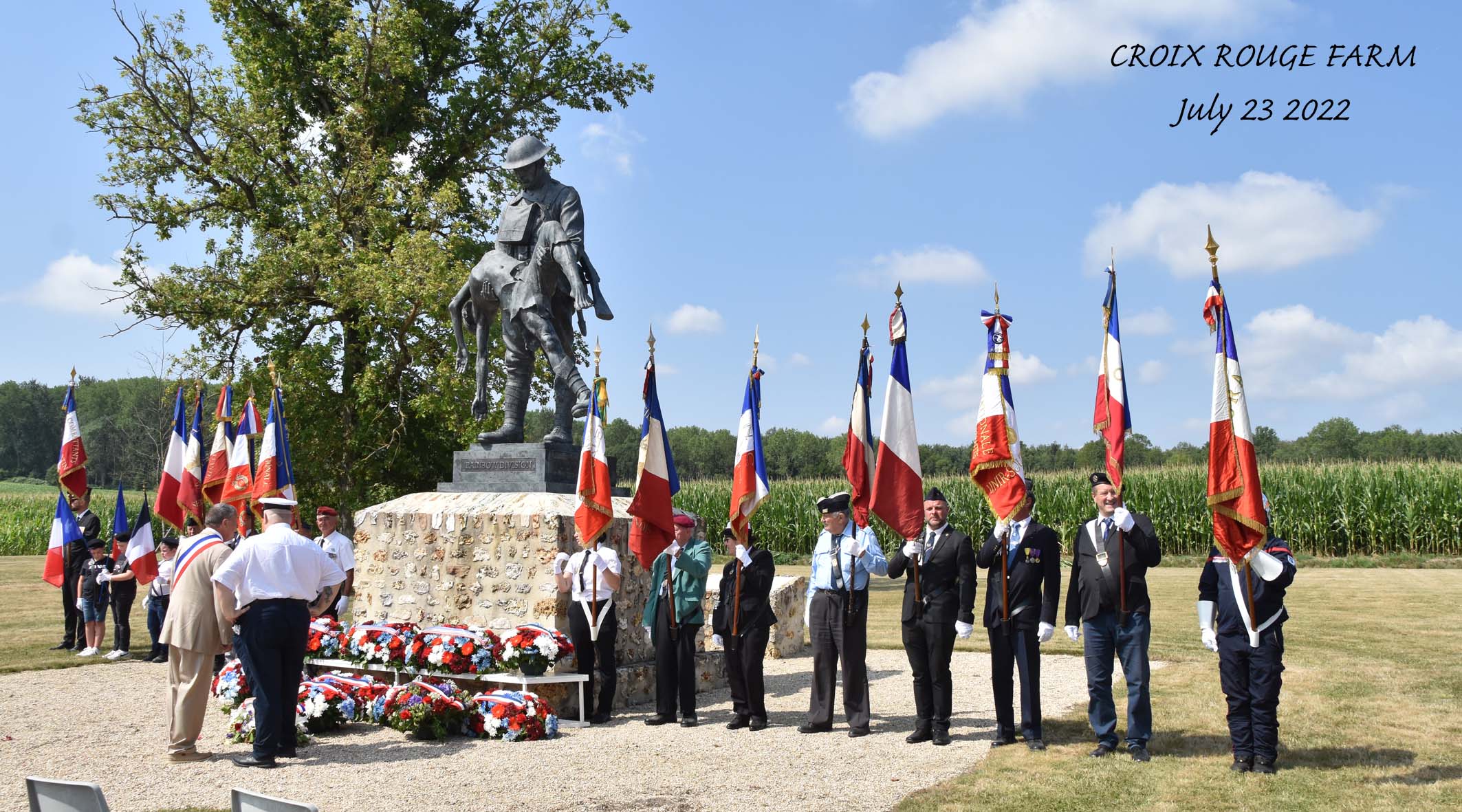 A wide shot of the wreaths at the base of the monument. Soldiers stand by with flags