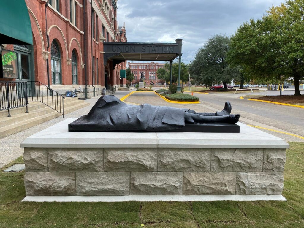 Side view of a statue of a dead returning soldier in front of a train station