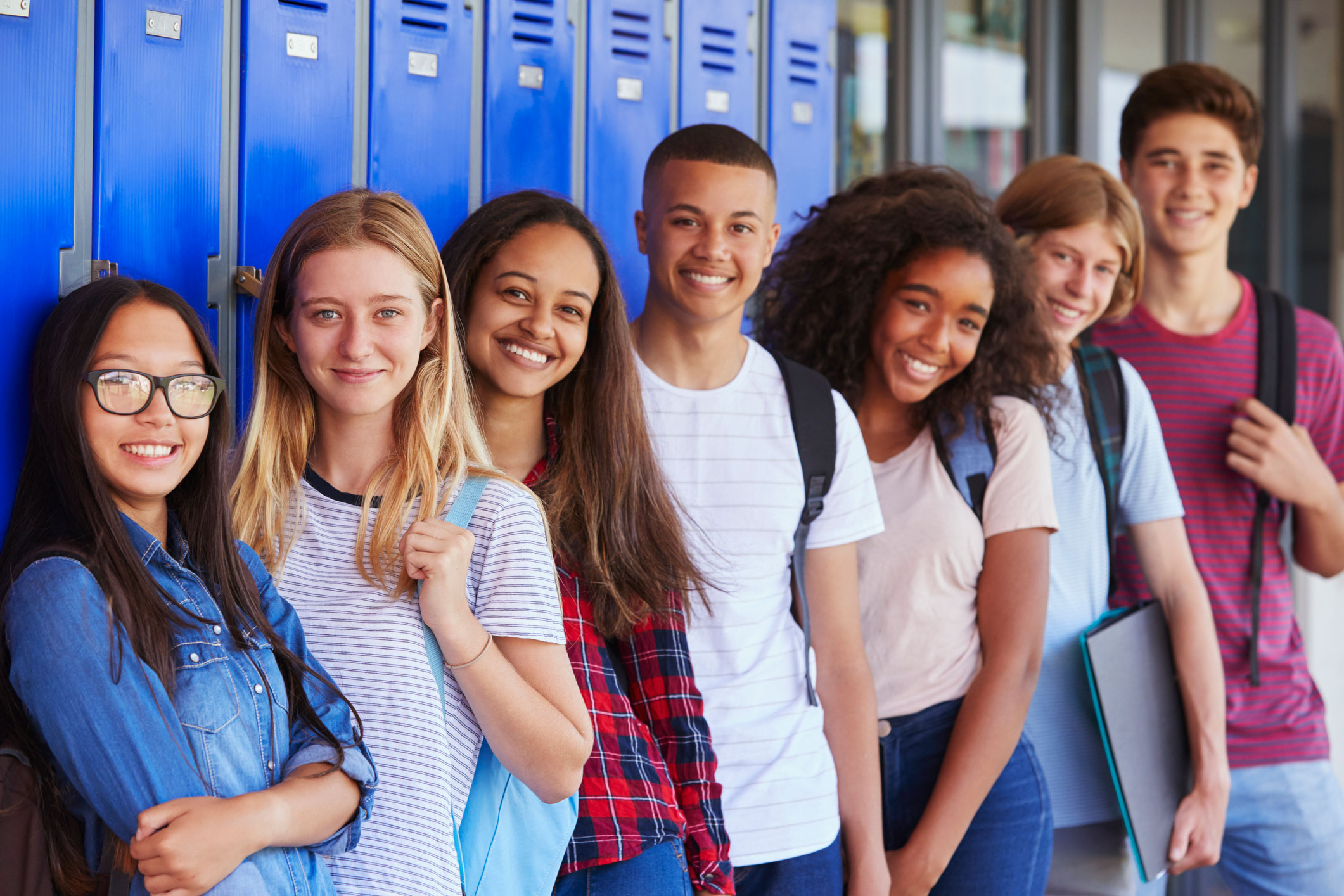 A group of seven teenage students in front of blue lockers.