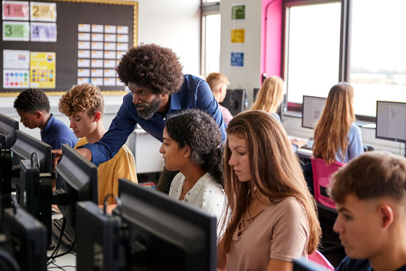 A teacher helps some teenage students at computers